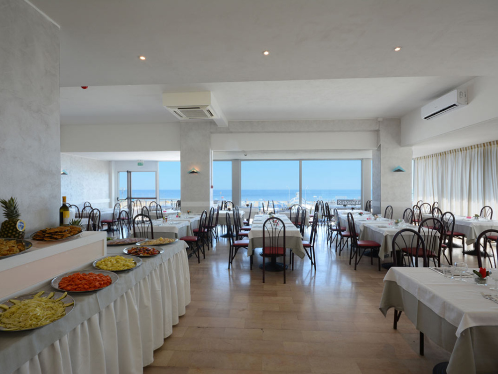 Ristorante elegante con vista mare, tavoli apparecchiati e buffet di antipasti.