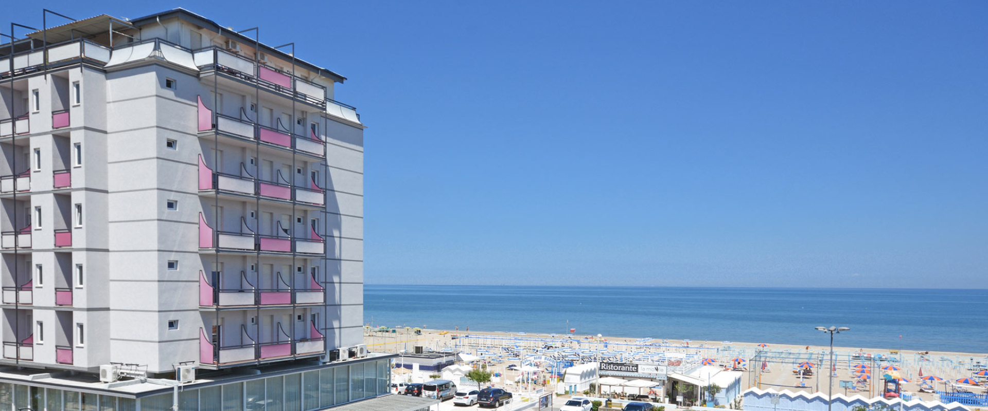 Hotel fronte mare con balconi rosa e vista sulla spiaggia e il mare.