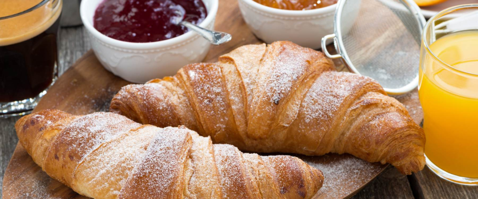 Colazione con croissant, caffè, succo d'arancia e marmellate su un tavolo di legno.