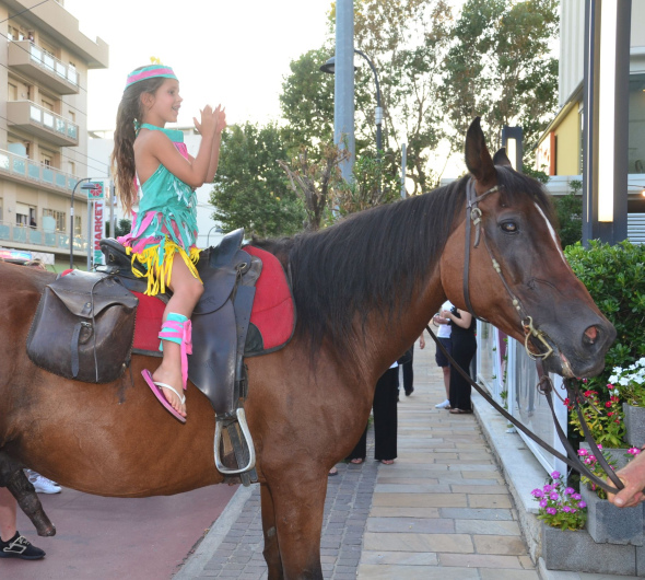 Bambina in costume colorato su cavallo, applaudita da passanti in città.