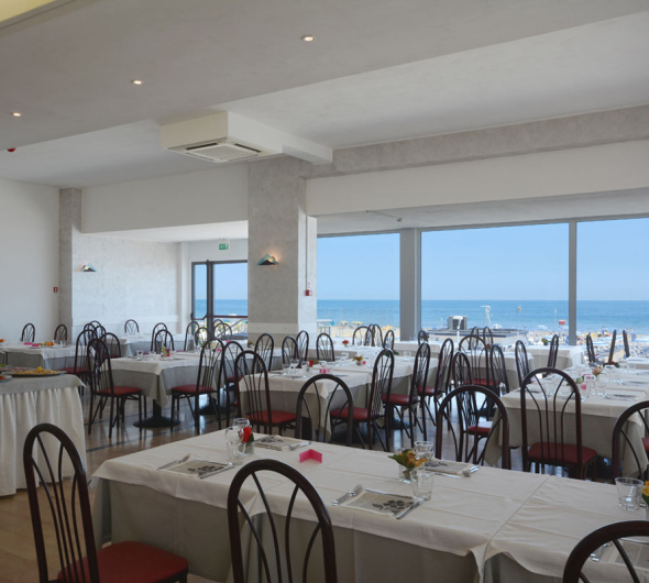 Ristorante elegante con vista mare, tavoli apparecchiati e ambiente luminoso.