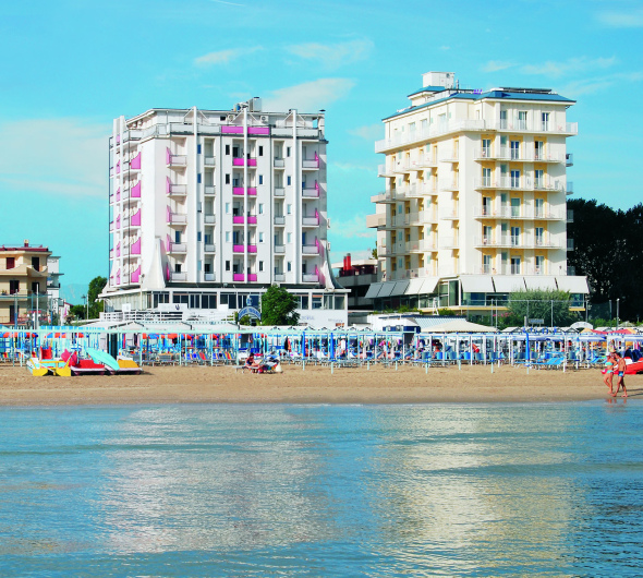 Spiaggia affollata con ombrelloni colorati e hotel sullo sfondo, cielo sereno.