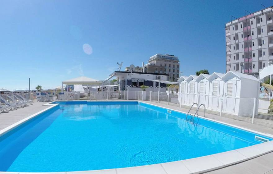 Outdoor pool with loungers and cabins on a sunny day.